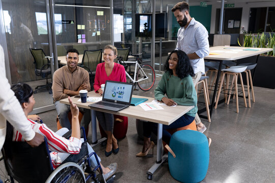 Happy biracial advisors listening to disabled businesswoman's strategy during meeting in boardroom
