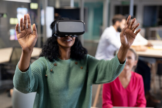 Smiling young african american businesswoman wearing virtual reality simulator gesturing in office