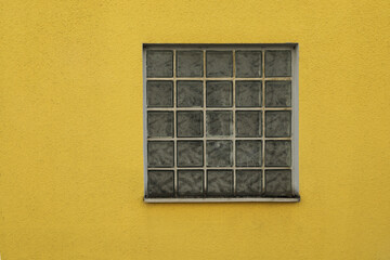 Yellow wall with glass brick window and grey concrete, close up, 
space for text no person