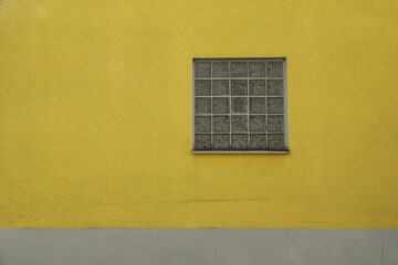 Yellow wall with glass brick window and grey concrete,
space for text no person