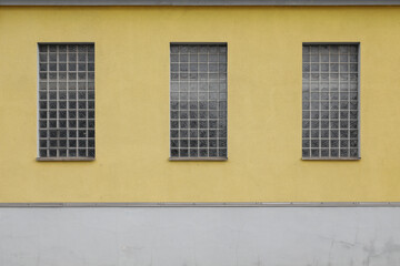 windows on a building, Three brick glass windows on a building, yellow painted wall with grey cement, no person