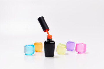 a black bottle with an orange varnish is slightly open on a white background along with multicolored cubes