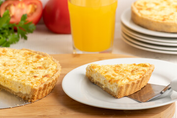 Cheese quiche, a pie on a wooden board, a slice of the pie on a white plate
