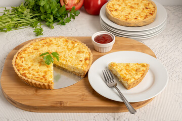 Cheese quiche, a pie on a wooden board, a slice of the pie on a white plate