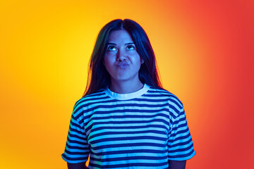 Portrait of young girl making funny faces, posing isolated over gradient orange yellow background in neon light