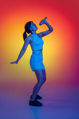 Fototapeta na wymiar Emotive young girl singing in microphone, performing isolated over multicolored background in neon light
