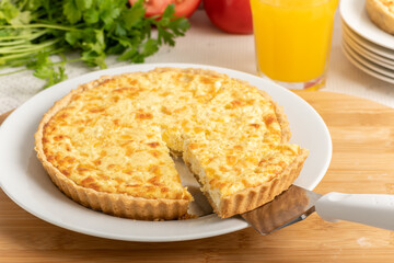Cheese quiche, a pie on a wooden board, a slice of the pie being taken out