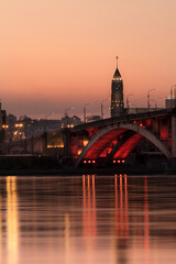 Krasnoyarsk at night - symbols of the city, a clock tower in the administration building, a communal bridge with red lighting and the flow of the river with a reflection in the water 
