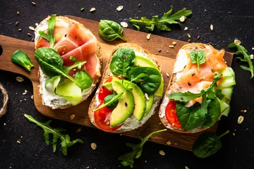 Foto op Canvas Open sandwich set with cream cheese, prosciutto, salmon, avocado and fresh greens. Top view at dark. © nadianb