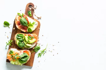 Foto op Canvas Open sandwichset met roomkaas, prosciutto, zalm, avocado en verse groenten. Bovenaanzicht aan witte tafel. © nadianb