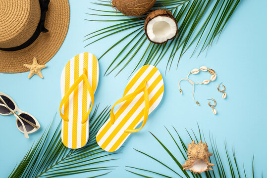 Summer vacation concept. Top view photo of sunhat yellow striped flip-flops sunglasses coconuts starfish shell bracelet earrings and palm leaves on isolated pastel blue background