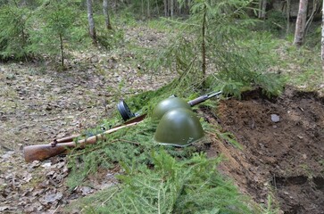 a wartime helmet and a machine gun lie on the edge of the trench