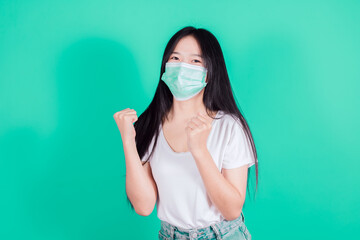 Happy Asian woman wears white t-shirt in medical face mask to protect Covid-19 (Coronavirus) raise hands glad excited cheerful on green background