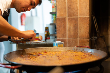 Young chef preparing paella in a large frying pan.