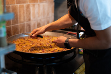 Young chef preparing paella in a large frying pan.