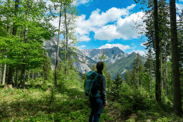 Woman with backpack standing on rock on a hiking trail in early spring with panoramic view on the mountain peaks of Hochschwab Region in Upper Styria, Austria. Forest in Alps, Europe. Karlhochkogel