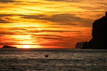 Panoramic sunset view from Marina Grande beach in Positano at Amalfi Coast, Italy, Campania, Europe. Silhouette of boat. Orange twilight over Li Galli islands in Mediterranean Sea. Reflection