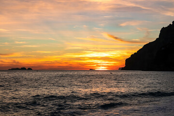 Panoramic sunset view from Marina Grande beach in Positano at Amalfi Coast, Italy, Campania, Europe. Silhouette of boat. Orange twilight over Li Galli islands in Mediterranean Sea. Reflection