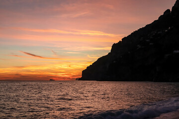 Panoramic sunset view from Marina Grande beach in Positano at Amalfi Coast, Italy, Campania, Europe. Silhouette of coastline. Orange twilight over Li Galli islands in Mediterranean Sea. Reflection