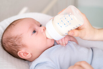 loving mother feeding her little boy child with milk baby bottle at home, portrait infant Baby...