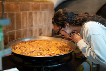 Beautiful young woman smelling delicious paella in a saucepan.