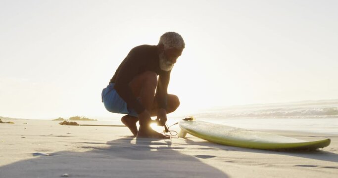 Senior african american man preparing before surfing on sunny beach