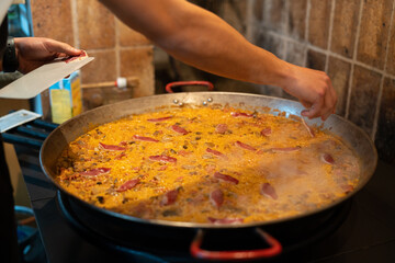 Young chef preparing paella in a large frying pan.