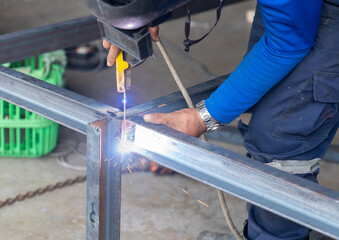 Worker welding leg of table with his hands, sparks without gloves.