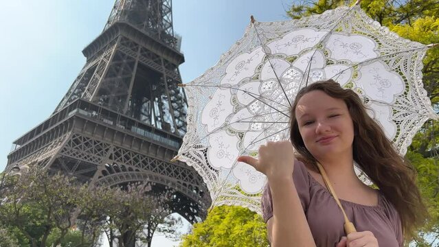 a cheerful teen girl stands against the backdrop of the Eiffel Tower she raised her hand, you can advertise a travel agency trip to Paris France. girls in the hands of an openwork umbrella