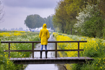 Young woman with yellow raincoat and rubber boots in spring nature