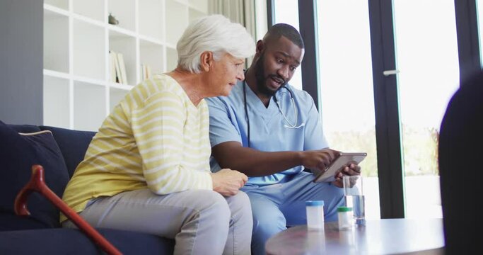Video of african american male doctor using tablet with caucasian senior woman