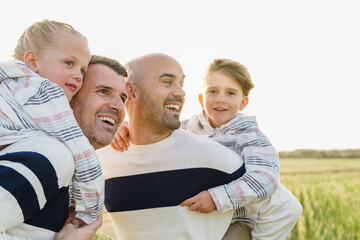 Gay male parents having fun with their sons outdoor in summer day - LGBT diversity family concept - Focus on left child face