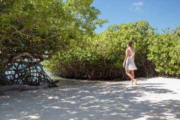 Fototapeta premium woman in white dress walking towards water on beach