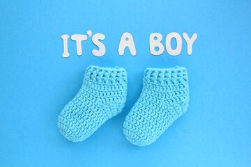 It's a boy lettering, crochet baby booties on blue background. Baby boy birth, new life, family concept. Greeting card idea for newborn. Pregnancy announcement. Flatlay, top view