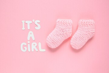 It's a girl lettering, crochet baby booties on pink background. Baby girl birth, new life, family concept. Greeting card idea for newborn. Pregnancy announcement. Flatlay, top view