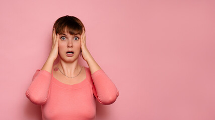 Portrait of a surprised attractive Caucasian girl isolated on a pink background, holding her head...
