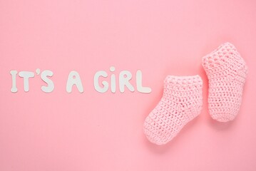 It's a girl lettering, crochet baby booties on pink background. Baby girl birth, new life, family concept. Greeting card idea for newborn. Pregnancy announcement. Flatlay, top view
