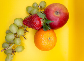 fruis, apple, strawberries, orange, grapes on a yellow background