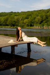 Young woman relaxing on the wooden pier at the calm lake