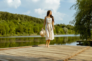 Young woman walking on the wooden pier at the calm lake