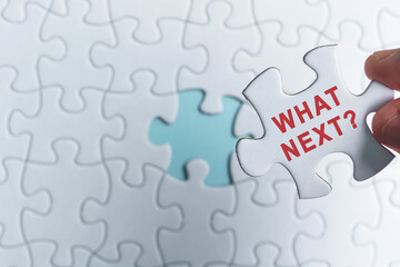 Hand holding piece of jigsaw puzzle with word What Next. Decision making concept