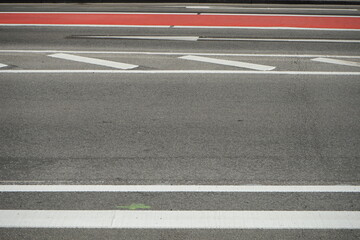 Weiße Fahrbahnmarkierung auf grauem Asphalt und Markierung in Rot für den Radweg bei Sonnenschein...