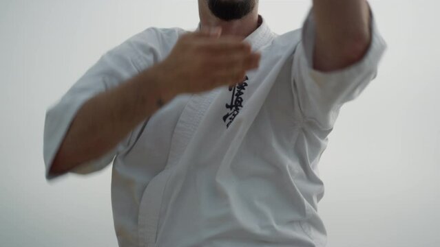 Sporty man exercising karate on beach close up. Fighter training matrial art.