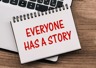 Everyone Has A Story text on notepad lying on a laptop on wooden table.