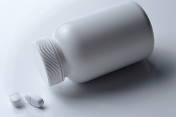 white plastic medicine jar and two white pills. light background