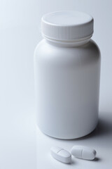 white plastic medicine jar and two white pills. light background