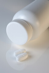 white plastic medicine jar and two white pills. light background