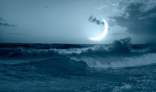 Night sky with blue crescent moon in the clouds - Rocky coastline with power sea wave