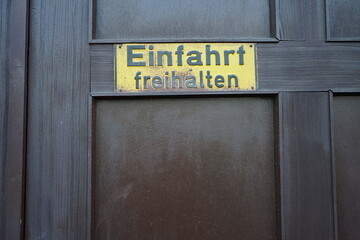 Rostiges gelbes Einfahrt freihalten Blechschild an einem alten braunen Holztor im Stadtteil...