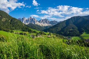 Fototapeta na wymiar Green grassy meadows in the village of Santa Maddalena against the great peaks of the Odle Group, Val di Funes, Dolomites.